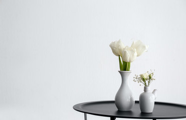 Vases with beautiful flowers on table against white background