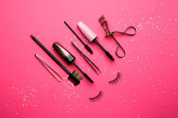 Mascara with false eyelashes and tools on color background