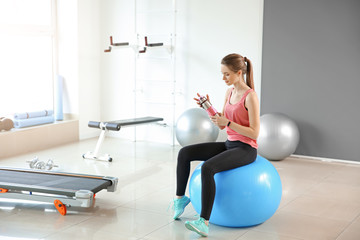 Fototapeta premium Sporty young woman drinking water in gym