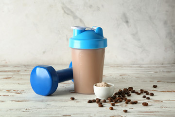 Bottle of protein shake with dumbbell on white wooden table