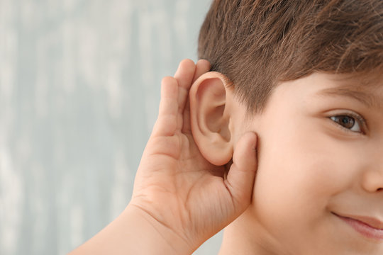 Little boy with hearing problem on grey background, closeup