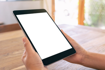Mockup image of a woman holding black tablet pc with blank white screen on wooden table