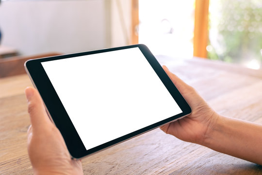 Mockup image of a woman holding black tablet pc with blank white screen horizontally on wooden table