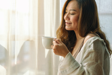 Closeup image of a beautiful asian woman holding and smelling a cup of hot coffee with feeling relaxed in the morning