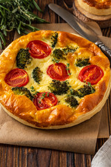 Vegetable pie with broccoli, peas, thyme. tomatoes and cheese on wooden background. Copy space.