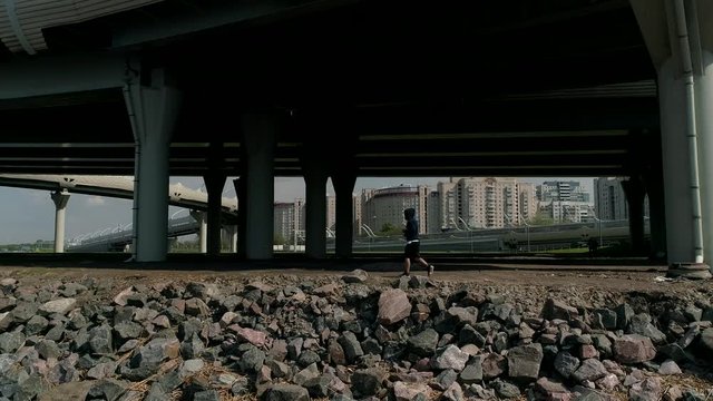 Aerial view man outdoor running with industrial street background. Man in hoodie and snapback running under interchange construction.