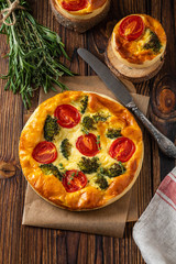 Vegetable pie with broccoli, peas, thyme. tomatoes and cheese on wooden background. Copy space.