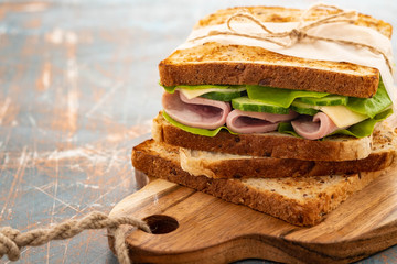 Close-up photo of a club sandwich. Sandwich with meet, prosciutto, salami, salad, vegetables, lettuce on a fresh sliced bread on wooden background. Copy space.