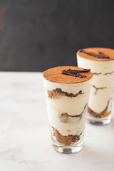 Homemade tiramisu, traditional Italian dessert in glass on white table. Copy space.