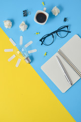 Financial planning table top with blank clip board, office supplies, pen, notepad, eyeglasses, coffee cup, light bulb on yellow and blue background. Conceptual brainstorming still life