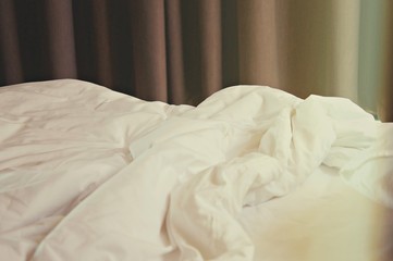 wrinkle messy blanket and white pillow in bedroom after waking up in the morning, from sleeping in a long night, details of duvet and blanket, an unmade bed in hotel bedroom with white blanket.