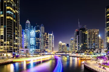 Gardinen Stunning view of the Dubai Marina at dusk with illuminated skyscrapers in the background and a light trails left by a yacht sailing in the foreground. Dubai, United Arab, Emirates. © Travel Wild