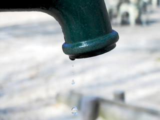 Metal green crane of the water pump with drop of water. The concept of water scarcity, drought and dry season.