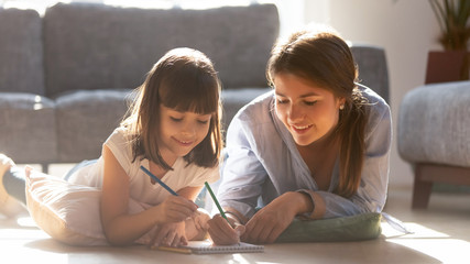 Mother drawing with daughter lying on warm floor