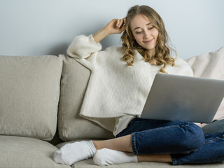 Girl sitting on sofa with laptope, hold big white mag cacao with marshmallow and listen music. Home...