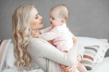 Young mother with her little cute baby daughter. Little baby girl and her mom. Mama with her child indoor.