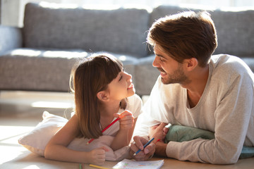 Father little daughter lying on floor drawing and talking