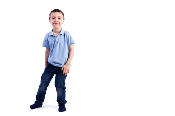 Little smiling boy with dark hair in blue jeans, blue polo t-shirt posing, laughing happily on a white isolated background in a photo studio. Portrait of happy joyful beautiful boy