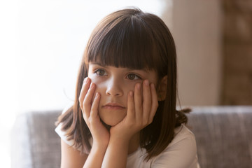 Upset little girl sitting on couch at home feels unhappy