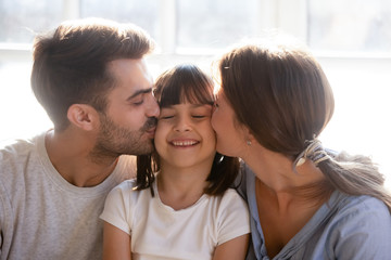 Fototapeta premium Happy parents kissing little preschool lovely daughter on cheeks