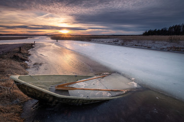 Scenic landscape with sunset and abandoned boat at spring evening in Finland. Boat is almoust in the ice.