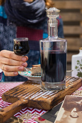 Woman hands holds deep red color liquor drink in shot glass and beautiful decanter on served table. is Alcoholic hard drink fermented with sugar.
