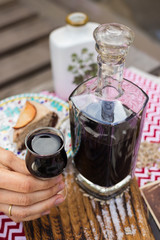 Woman hands holds deep red color liquor drink in shot glass and beautiful decanter on served table. is Alcoholic hard drink fermented with sugar.