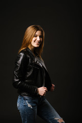 Young caucasian woman wearing a leather jacket and jeans posing on the black background