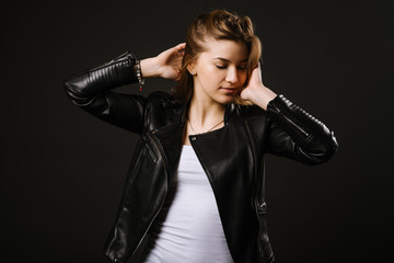 Young caucasian woman wearing a leather jacket and jeans posing on the black background