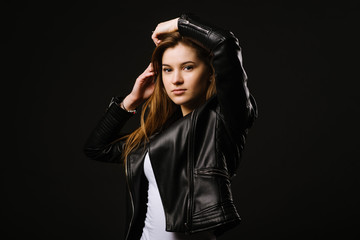 Young caucasian woman wearing a leather jacket and jeans posing on the black background