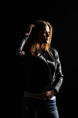 Young caucasian woman wearing a leather jacket and jeans posing on the black background