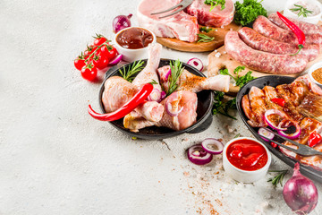 Various raw meat ready for grill and bbq, with vegetables, greens, sauces kitchen grilling utensils. Chicken legs, pork steaks, sausages, beef ribs with herbs, white concrete background copy space