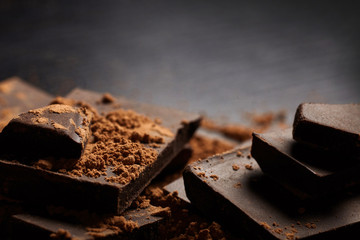 A pieces of dark chocolate and cocoa on black baackground..