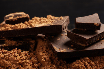 Broken dark chocolate and cocoa on black background.