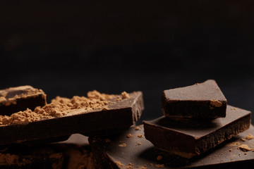 Broken dark chocolate and cocoa on black background.