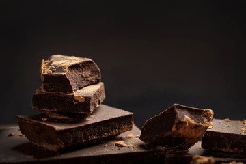 Broken dark chocolate and cocoa on black background.