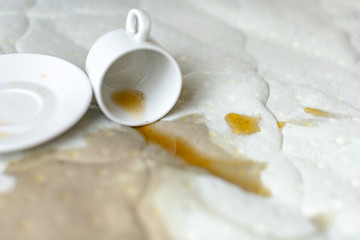Spilled cup of tea on the bed. Accidentally dropped cup with saucer on white bedsheet. Unlucky,...