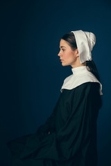 Heavy thoughts. Medieval young woman as a nun in vintage clothing and white mutch sitting on the...