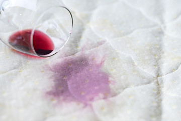 Wine glass spilled on bed. Dropped wineglass on white bed sheet. Pink wet stain. Unlucky,...