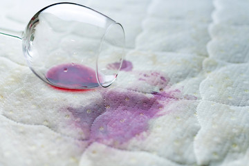 Spilled wine glass on the bed. Accidentally dropped wineglass on white bedsheet. Unlucky,...