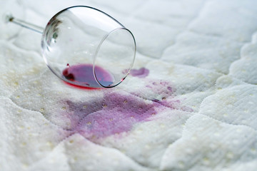 Spilled wine glass on the bed. Accidentally dropped wineglass on white bedsheet. Unlucky,...