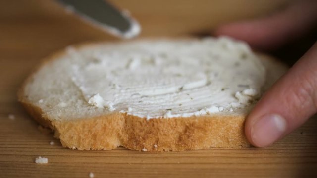 Man spreading butter on rye dry toast with a knife. Person spreading creamy butter on a piece of bread. Close up of male hands spreading butter on bread in kitchen,  slow motion.