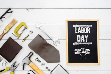 Labor day background concept. Flat lay of construction blue collar handy tools and white collar's accessories over wooden background with black chalkboard and Labor Day text.