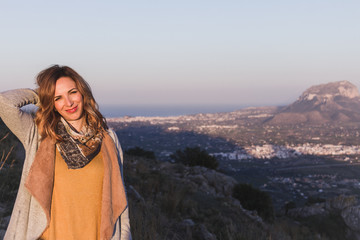 Naklejka premium Portrait of a young woman with ochre colored clothes, posing in a beautiful landscape at sunset. Montgo mountain is in the background, in Spain