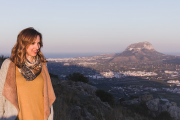 Naklejka premium Portrait of a young woman with ochre colored clothes, posing in a beautiful landscape at sunset. Montgo mountain is in the background, in Spain