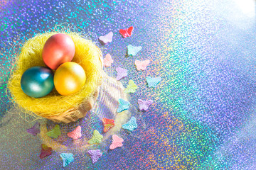 Easter. Multicolored Painted eggs of yellow, pink, green, turquoise pearl color in a basket on a holographic rainbow background with a copy space