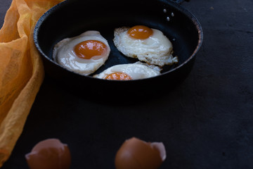 Overhead view of  fried eggs in black baking pan on dark background