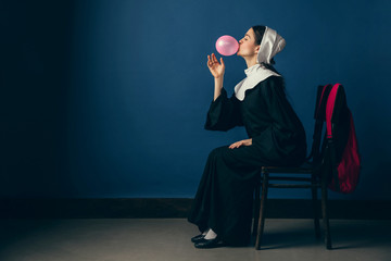 Light touch of youth. Medieval young woman as a nun in vintage clothing, white mutch and red bag...