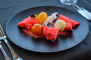 Red desert with macaron on black plate in restaurant.