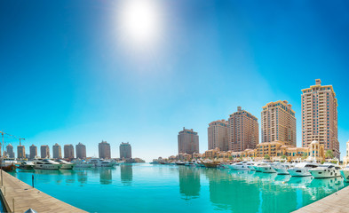 Fototapeta na wymiar Panorama of luxury residential buildings of Pearl Qatar and white yachts at Porto Arabia marina. Doha, Qatar